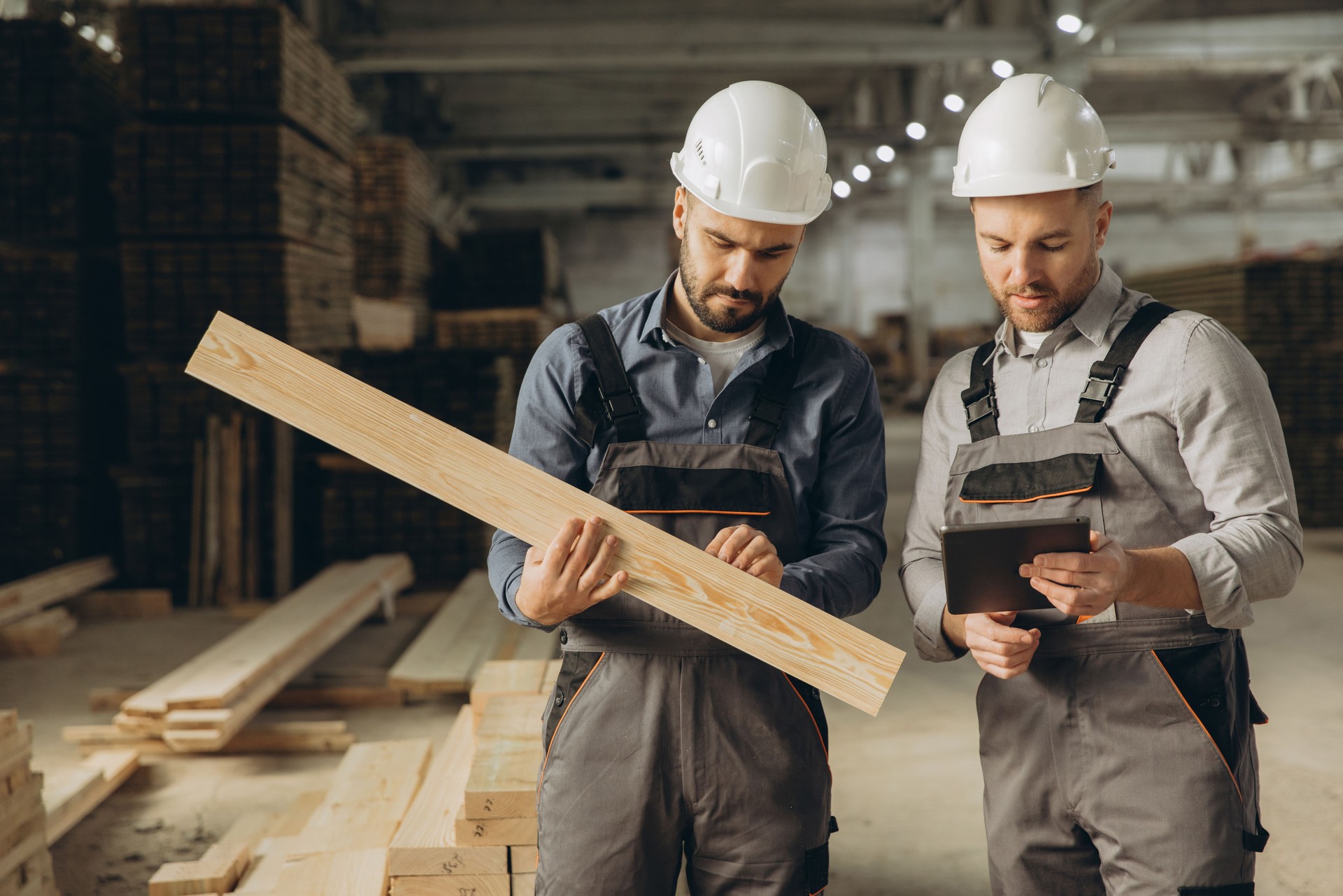 Construction workers inspecting lumber and using digital tablet in warehouse